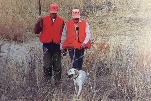 walking two men wearing orange vests hunting with dog